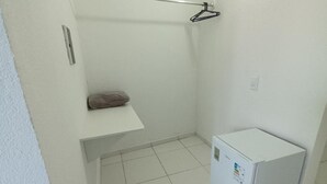 A small, white-walled room with a white tiled floor, a white washing machine, and a small shelf with a brown item on it.