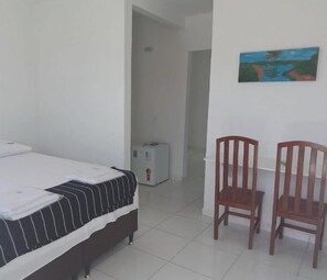 Une chambre à coucher avec un lit, deux chaises en bois, un tableau au mur et un sol carrelé de carreaux blancs.