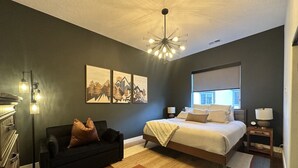 A bedroom with a bed, a nightstand, a dresser, a sofa, and a chandelier.