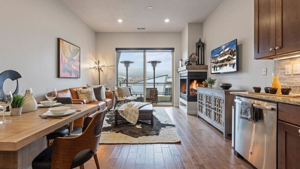 A modern kitchen with a dining area, a fireplace, and a large window overlooking a snowy landscape.