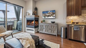 A modern kitchen with a fireplace, wooden cabinets, and a large window overlooking a snowy landscape.