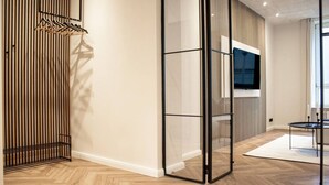 Un interior moderno con suelo de madera, un televisor montado en la pared y un separador de vidrio.