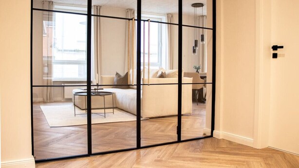 Una sala de estar moderna con un amplio separador de vidrio, piso de madera y un sofá con cojines.