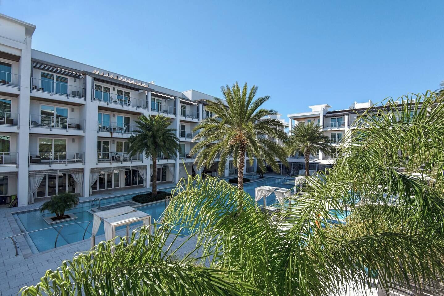 A hotel with multiple balconies, a swimming pool, and palm trees.
