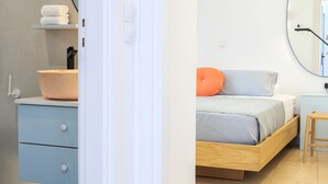 A bedroom with a bed, a bedside table, a mirror, and a bathroom with a sink and towel rack. - rodakino - Seafront Apartment (Agia Effimia)