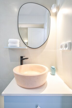 Une salle de bain avec un lavabo rond de couleur claire, un robinet noir, un miroir et un porte-serviettes avec des serviettes pliées.