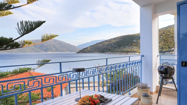 A balcony with a table set for a meal, overlooking a body of water and hills. - rodakino - Seafront Apartment (Agia Effimia)