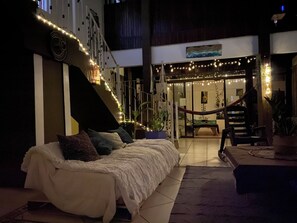 Uma área de estar ao ar livre aconchegante com sofá, cadeiras, escadas e luzinhas.