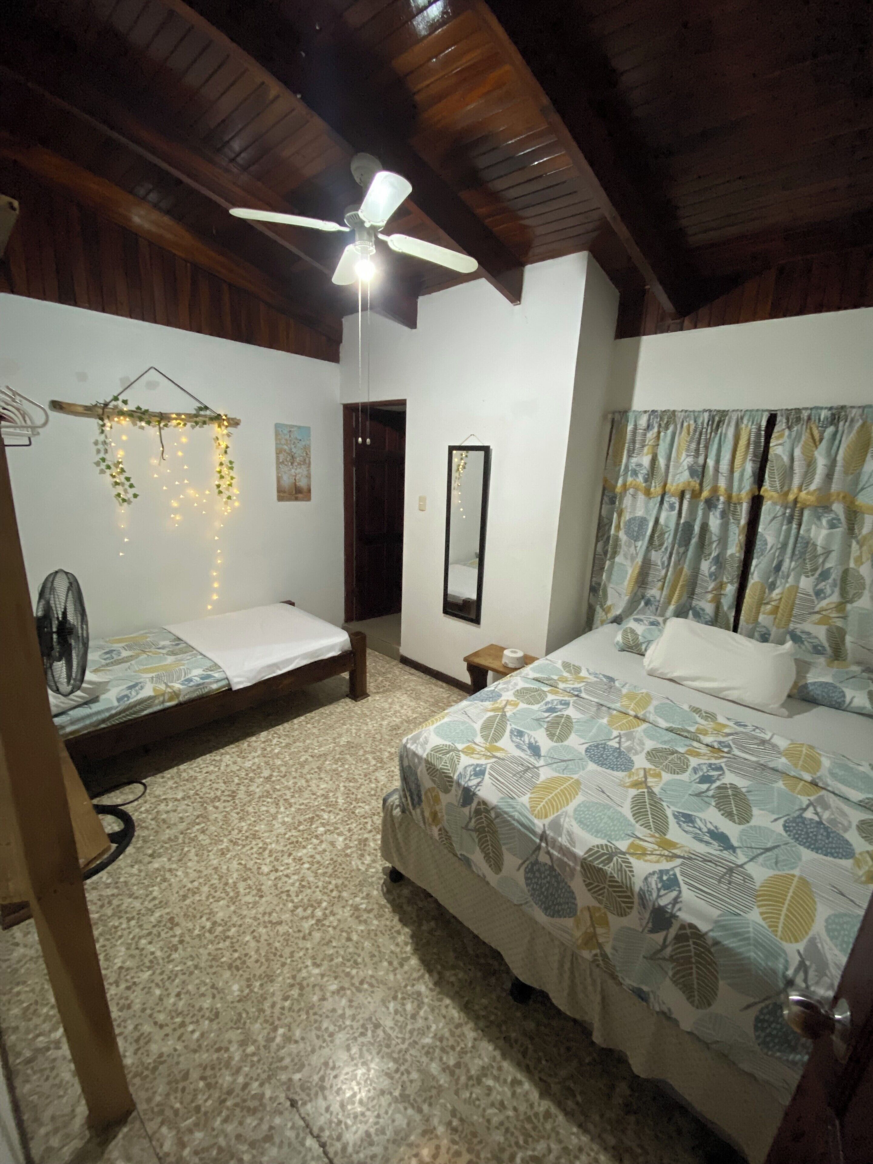 Un dormitorio con una cama, un ventilador, un ventilador de techo y una lámpara de pared.