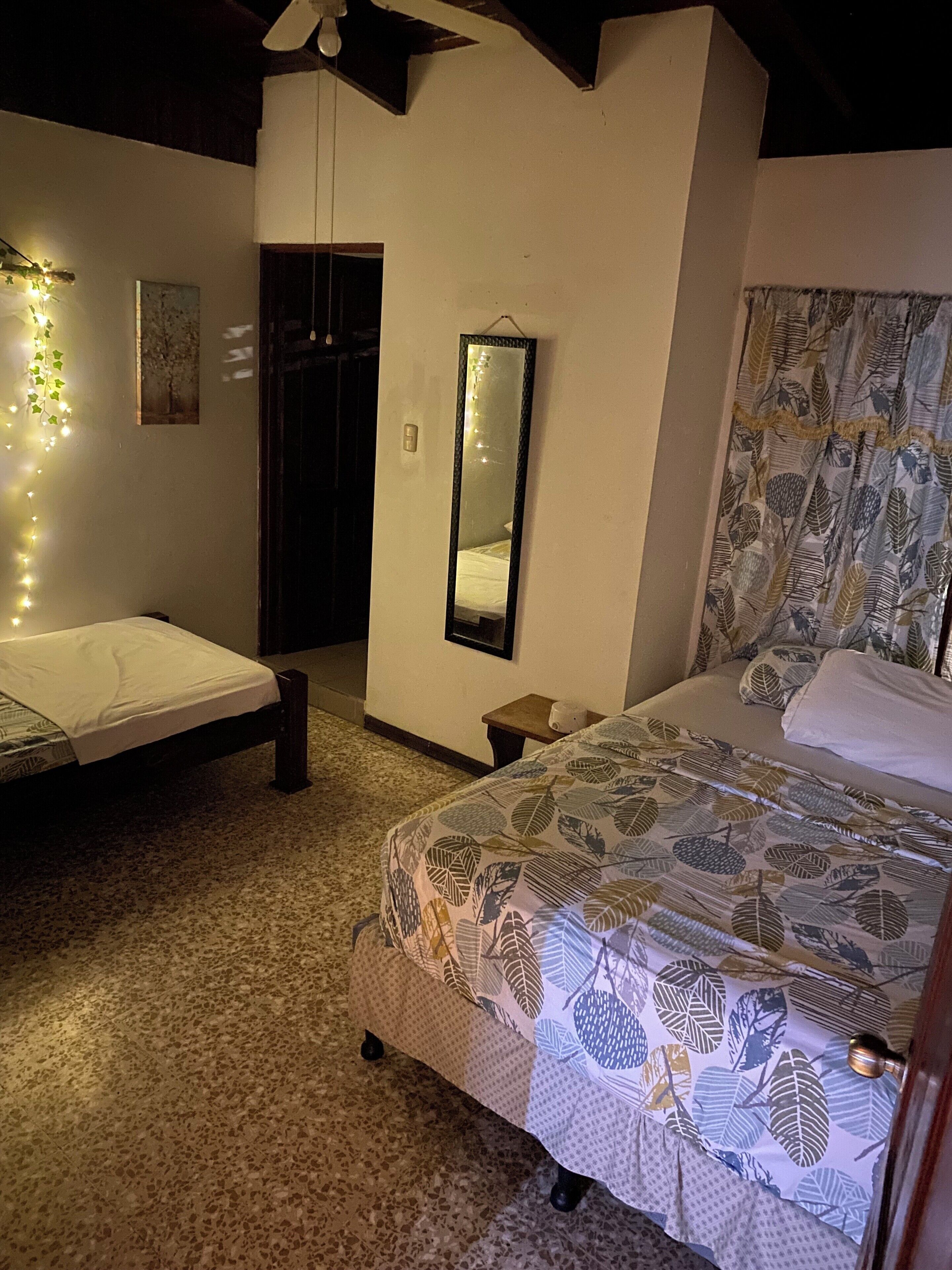 Un dormitorio con cama, espejo, una mesita y una lámpara de pared.