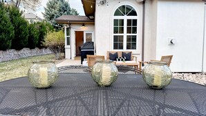 Une terrasse avec une table ronde en métal, quatre vases en verre et du mobilier d’extérieur.