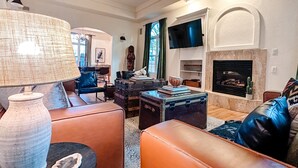 Un salon avec des canapés en cuir, une table basse, une cheminée et un téléviseur fixé au mur.