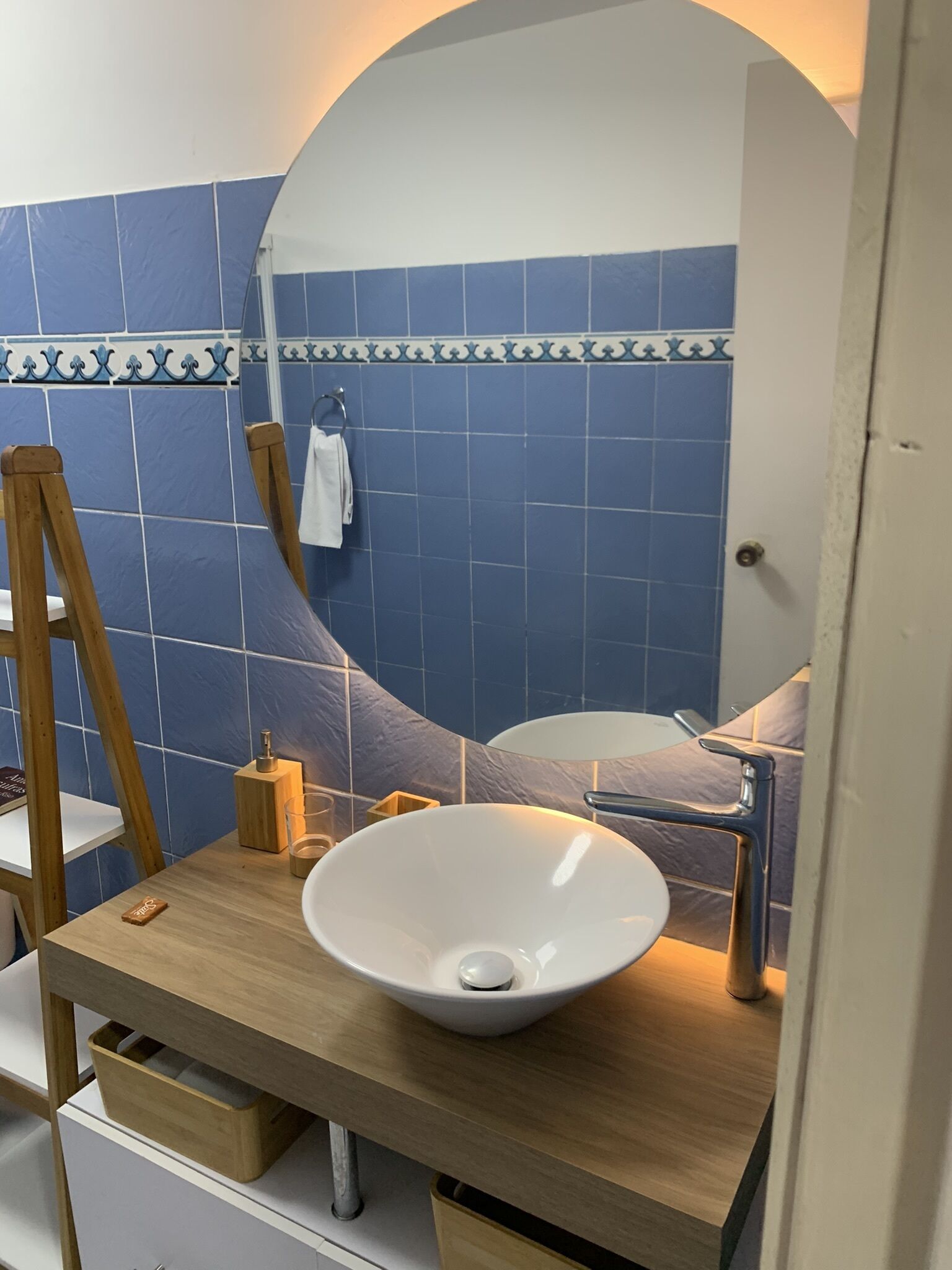 A bathroom with a white sink, wooden vanity, and blue tiled walls.