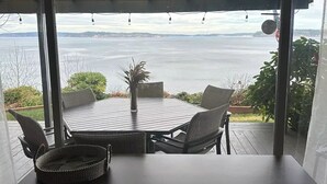 A covered outdoor dining area with a table and chairs, overlooking a body of water.
