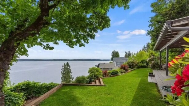 A well-maintained lawn with a wooden deck and a pergola, overlooking a body of water.