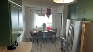 A compact kitchen with a dining table, chairs, a refrigerator, and a hanging light fixture.