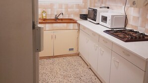Pieni, käytännöllinen keittiö, jossa on valkoiset kaapit, pesuallas, mikroaaltouuni ja liesi.