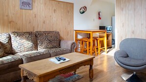 A cozy living room with a wooden sofa, a wooden coffee table, a gray armchair, and a wooden dining table with chairs. - Located on the river, facing the Mountains (Red River)