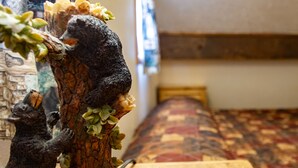 A room with a bed, a wooden table, and a bear figurine on the table. - Located on the river, facing the Mountains (Red River)