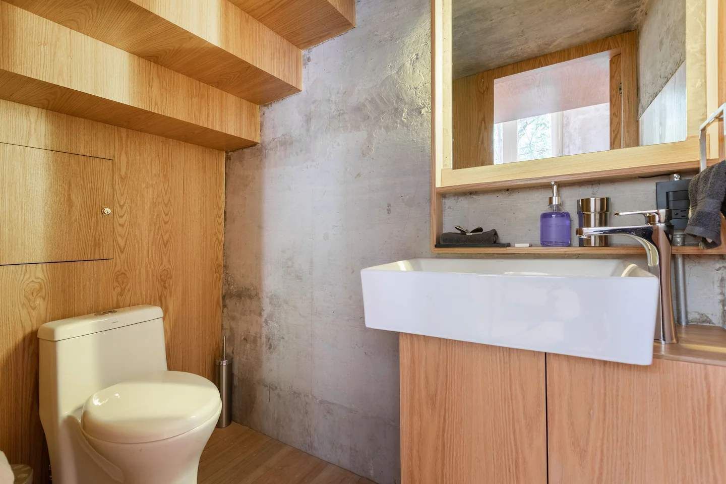 A modern bathroom with a toilet, a white sink, and wooden cabinetry.