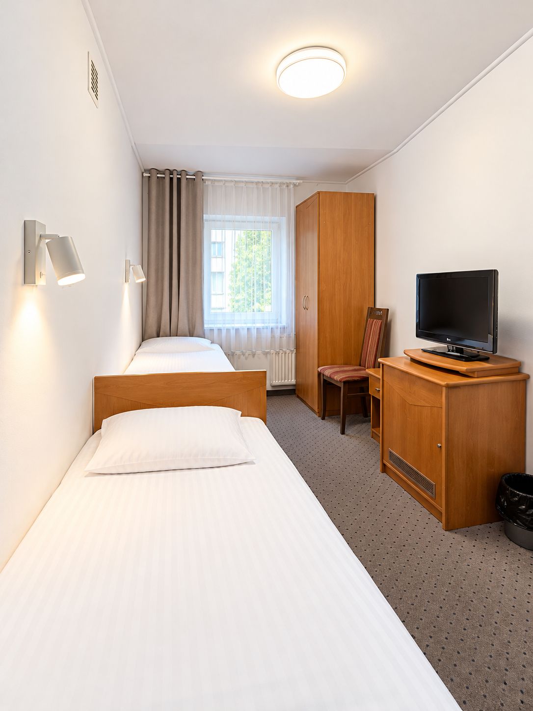 Hotellihuone, jossa on kaksi erillistä sänkyä, puinen vaatekaappi, televisio ja tuoli.