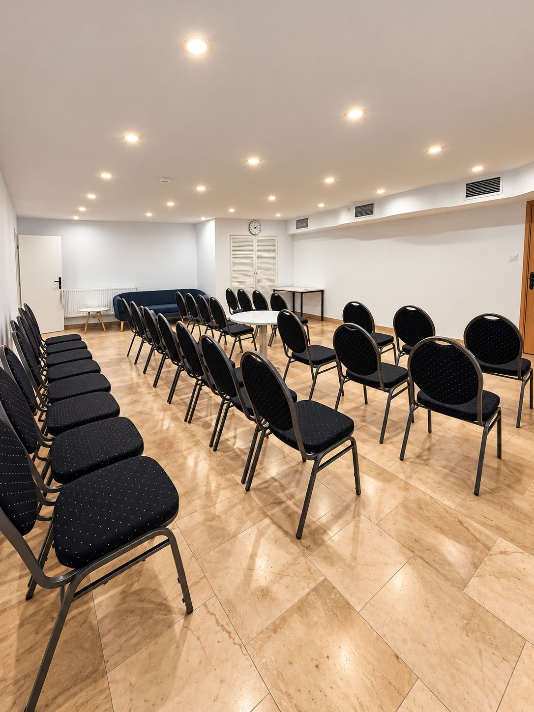 Un salón de conferencias con filas de sillas, una mesa y un reloj en la pared.