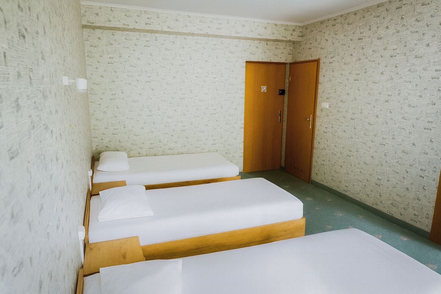 A room with two single beds, a wooden wardrobe, and a patterned wallpaper.