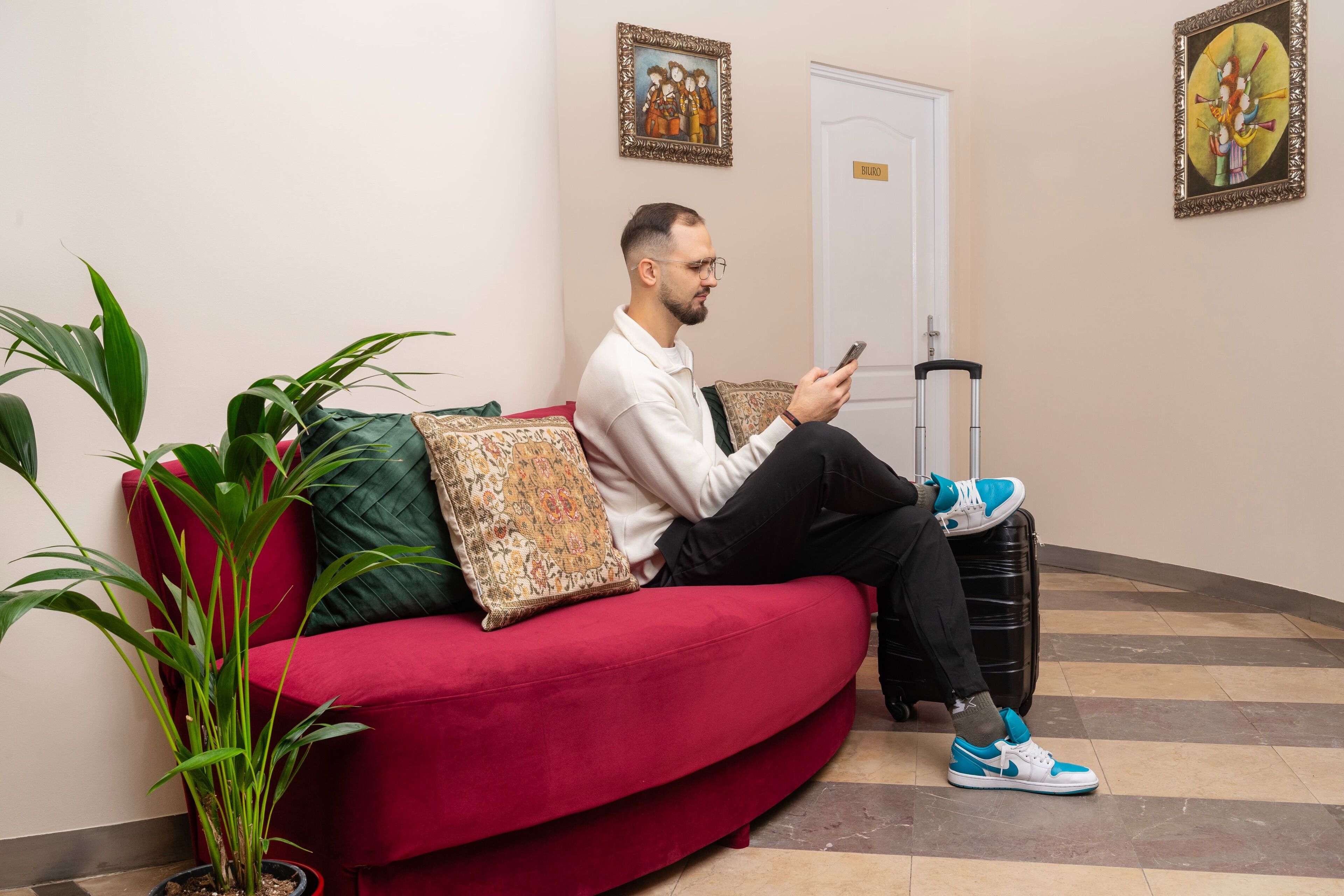 A person sitting on a red sofa with a suitcase, using a mobile phone.