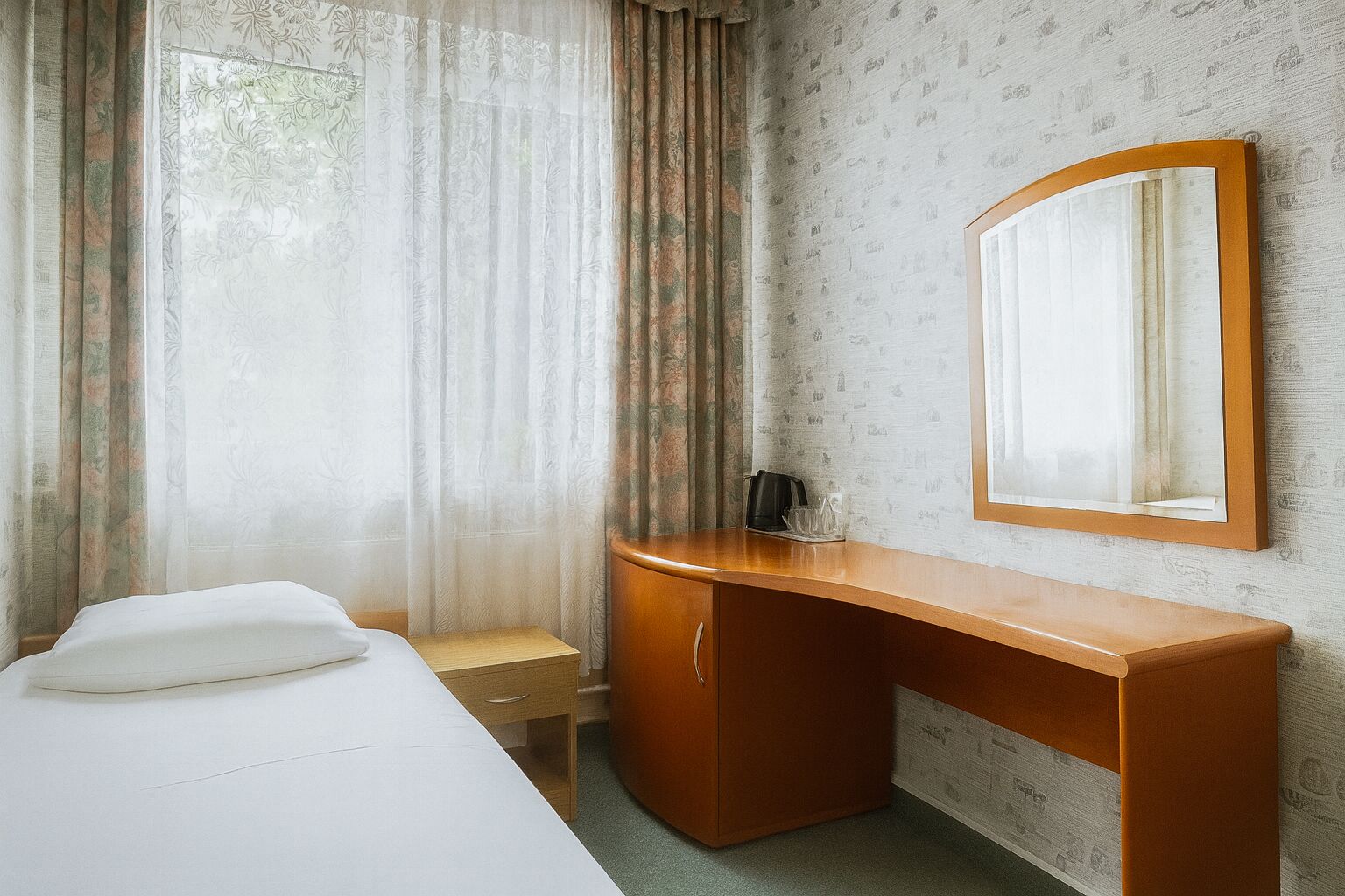 A hotel room with a bed, a wooden desk, a chair, a coffee maker, and a mirror on the wall.