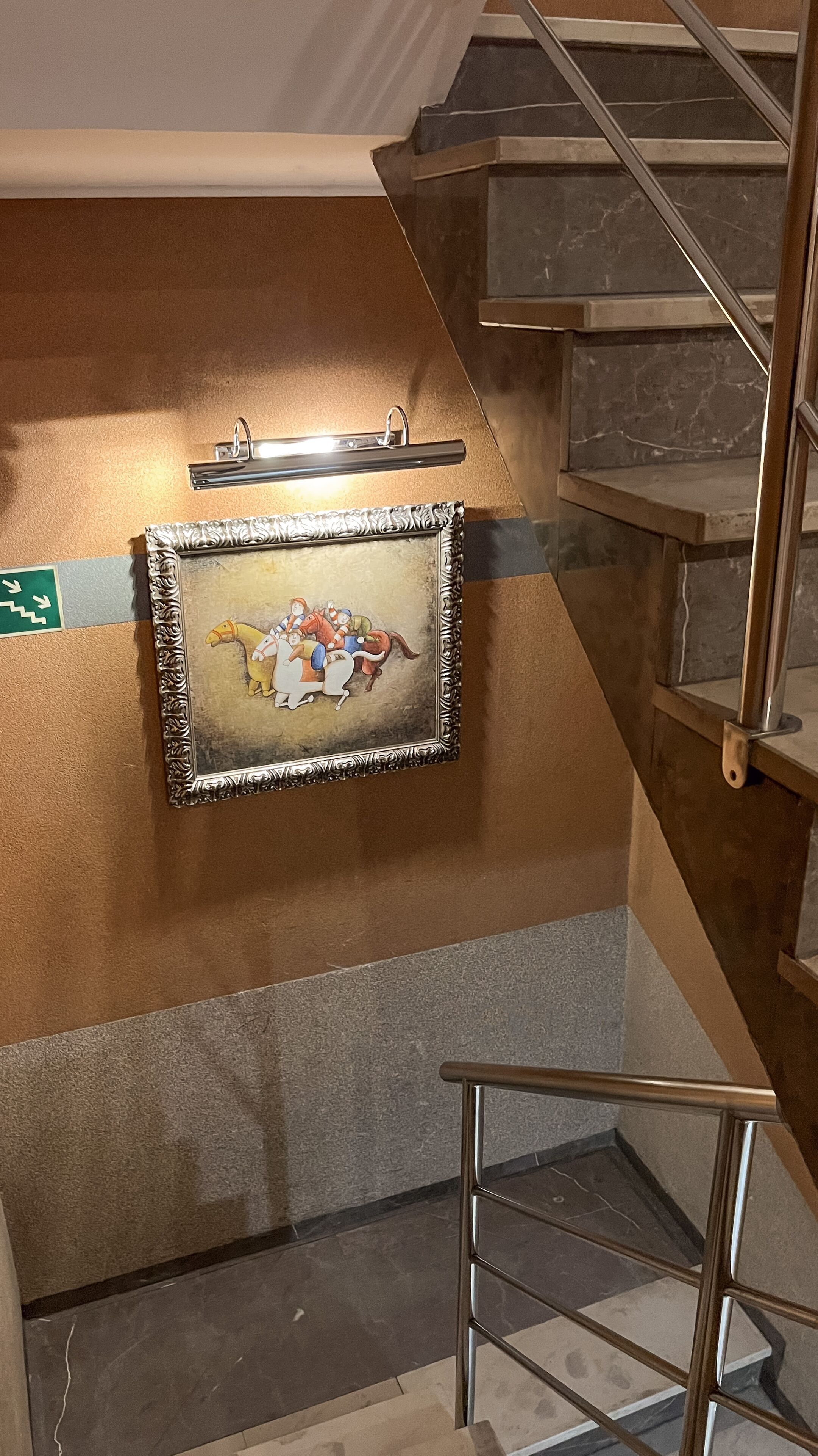 Un escalier avec une rampe en métal, un cadre photo fixé au mur et un panneau de signalisation vert.