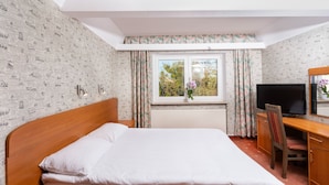 Una habitación de hotel con cama, escritorio con silla, televisor y ventana con cortinas.