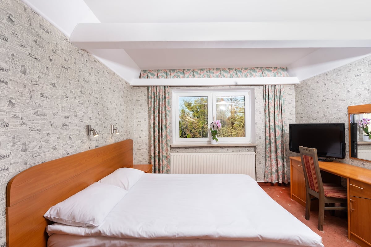 A hotel room with a bed, a desk with a chair, a television, and a window with curtains.