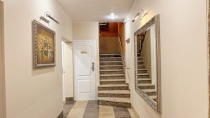 Un pasillo con una puerta blanca, una escalera de piedra y dos espejos grandes en las paredes.