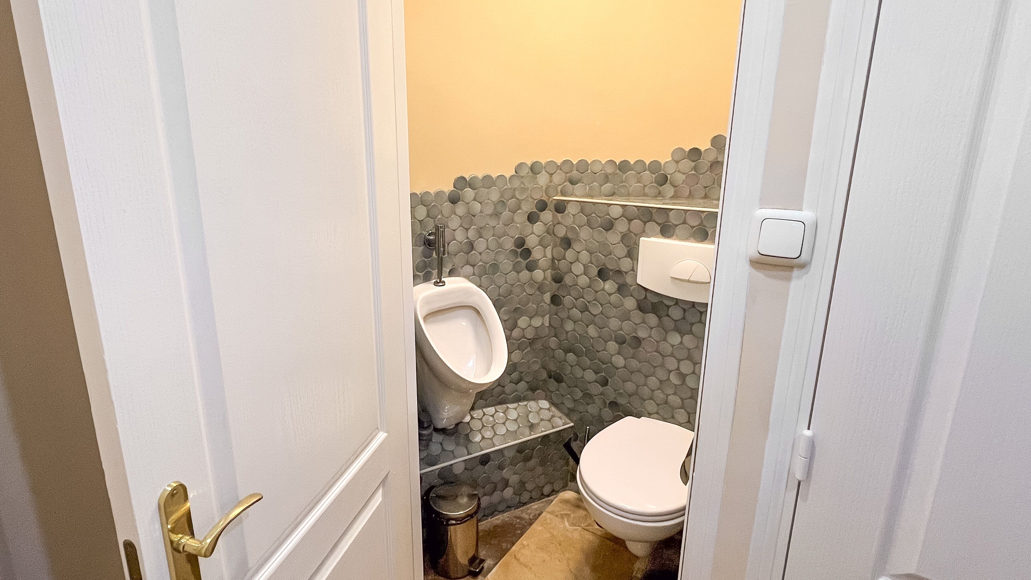 Une petite salle de bain compacte, équipée d’un urinoir, de toilettes et d’une poubelle.