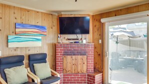 Een woonkamer met een televisie, twee stoelen, een open haard en uitzicht op de achtertuin.