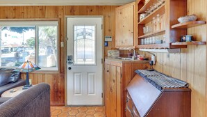 Een houten interieur met een deur, een klein kitchenette en een zithoek met een tafel en een lamp.