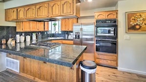A kitchen with wooden cabinets, a granite countertop, stainless steel appliances, and a trash can.