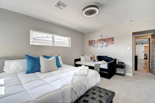 Une chambre moderne avec un grand lit, un canapé et une petite table. Une fenêtre laisse entrer la lumière naturelle et une œuvre d’art orne le mur.