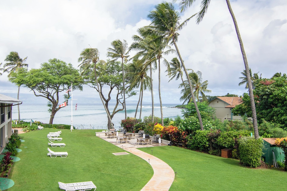 A hotel with a lawn, lounge chairs, and a view of the ocean.
