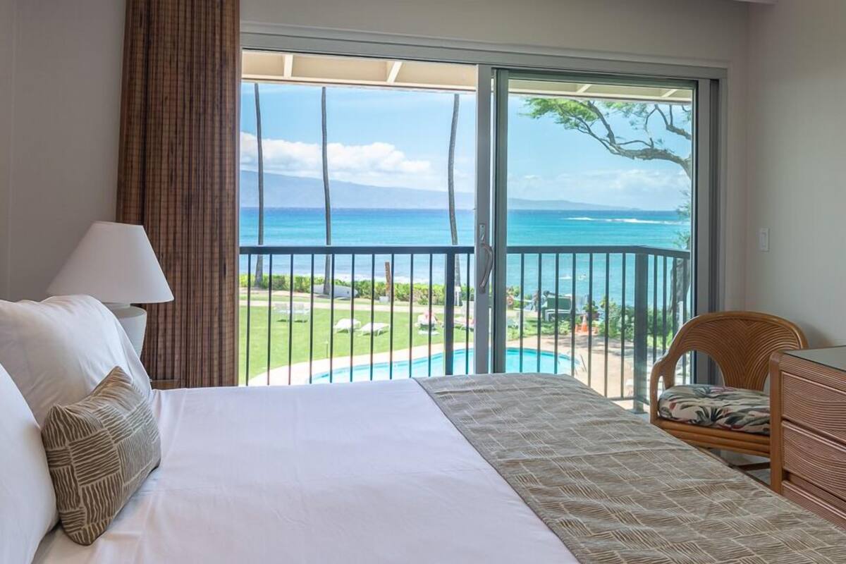 Une chambre d’hôtel avec un grand lit, une chaise, une commode et un balcon offrant une vue sur l’océan et la piscine.