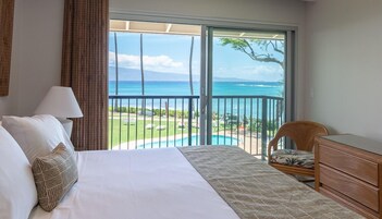 Quarto de hotel com uma cama grande, uma poltrona, cômoda e varanda com vista para o mar e piscina.