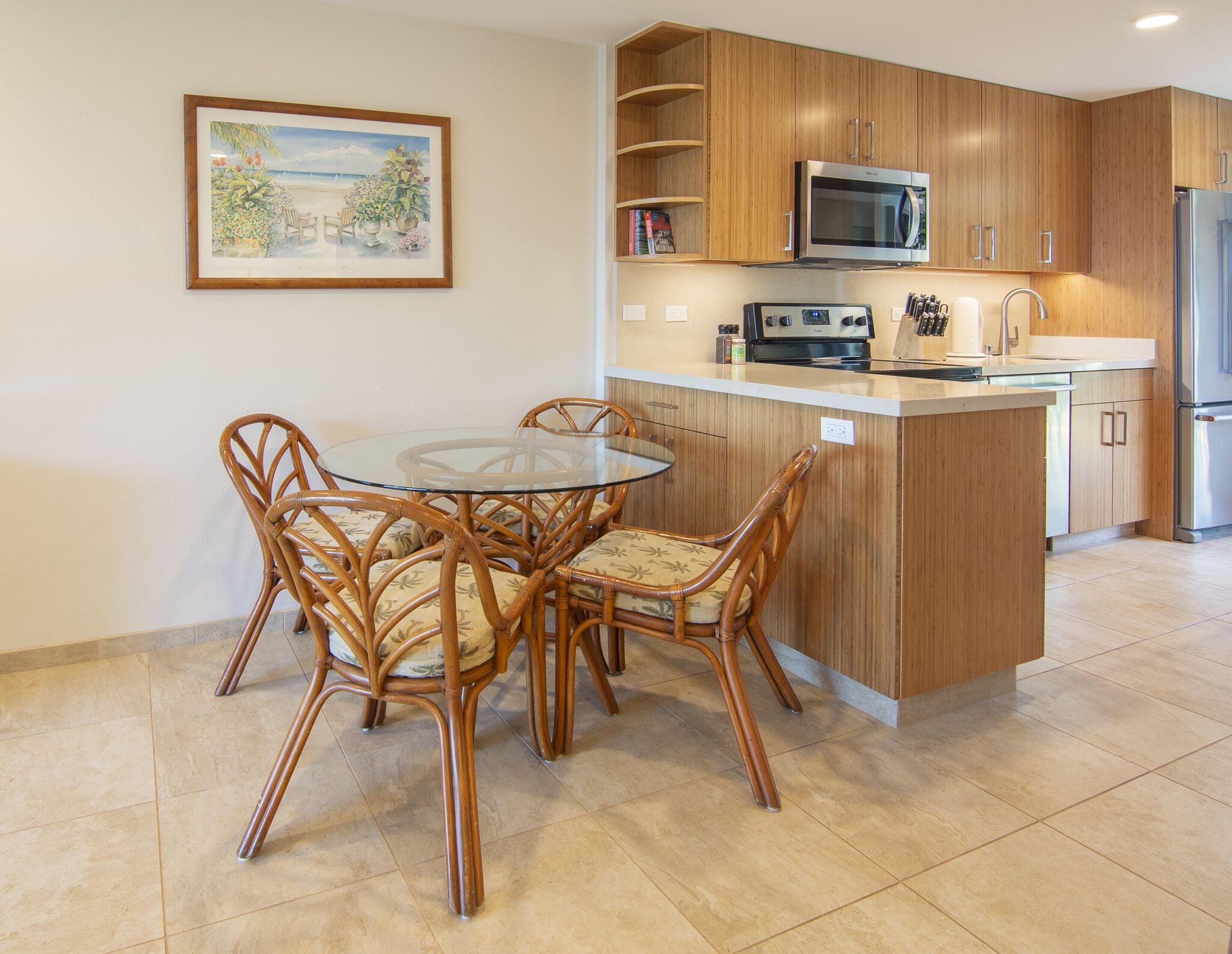 A kitchen with wooden cabinets, a microwave, a refrigerator, and a dining area with wicker chairs and a glass table.