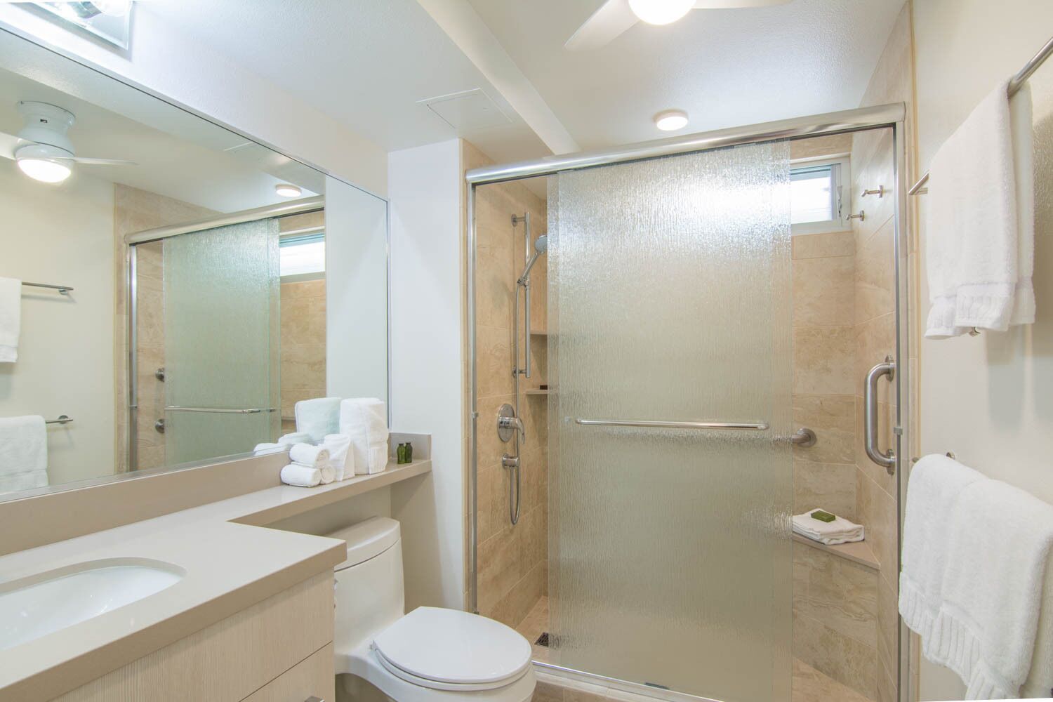 Un baño moderno con ducha de vidrio, inodoro, lavamanos con espejo y toallero.