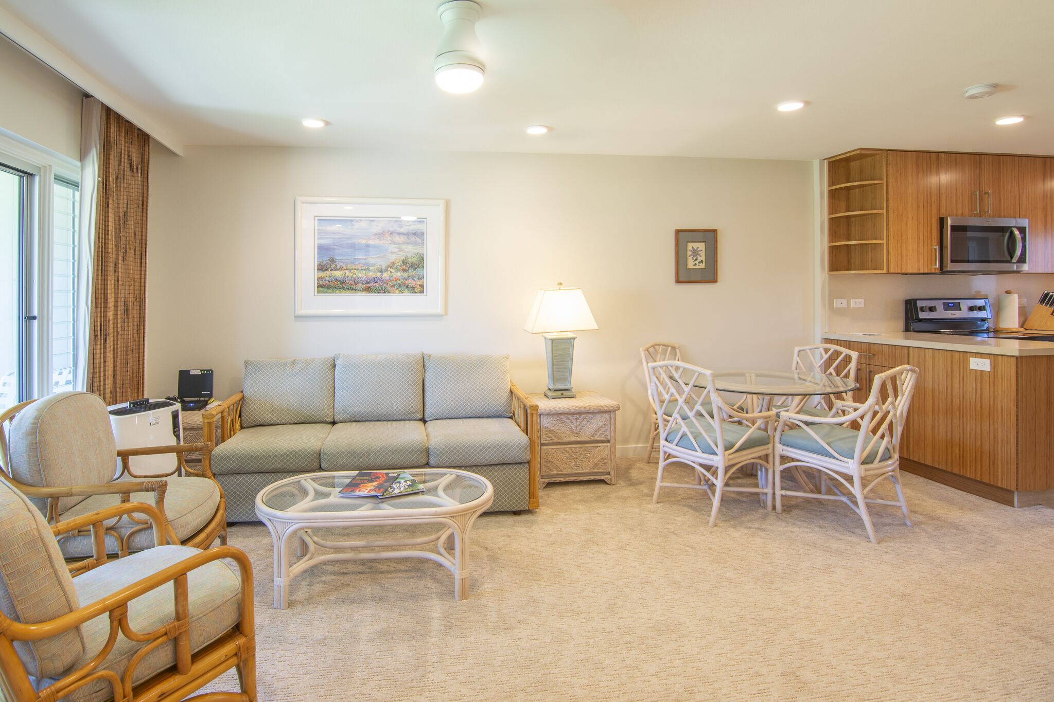 A living room with a sofa, chairs, a coffee table, and a dining table with chairs. There is a kitchen area with a microwave and cabinets.
