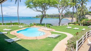 A swimming pool with lounge chairs, surrounded by palm trees and a view of the ocean.