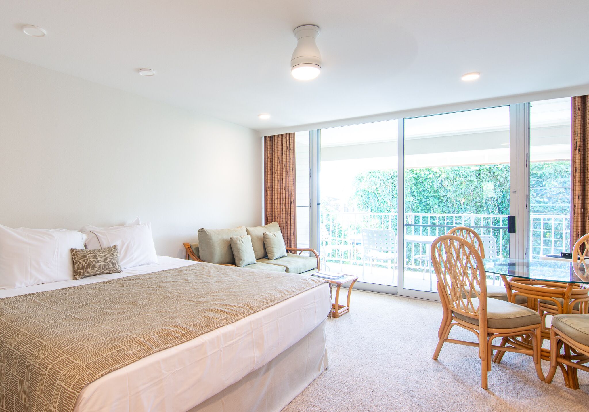 Una camera d'hotel con un letto grande, una zona salotto con un tavolo e un balcone vista verde.