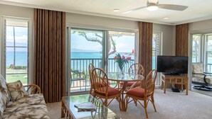 A spacious living room with a balcony overlooking the ocean, furnished with a sofa, chairs, and a coffee table.