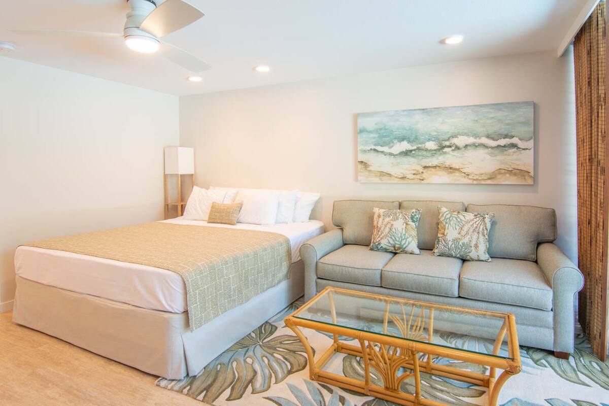 Une chambre à coucher avec un lit, un canapé, une table basse en verre et un tableau représentant une scène de plage.