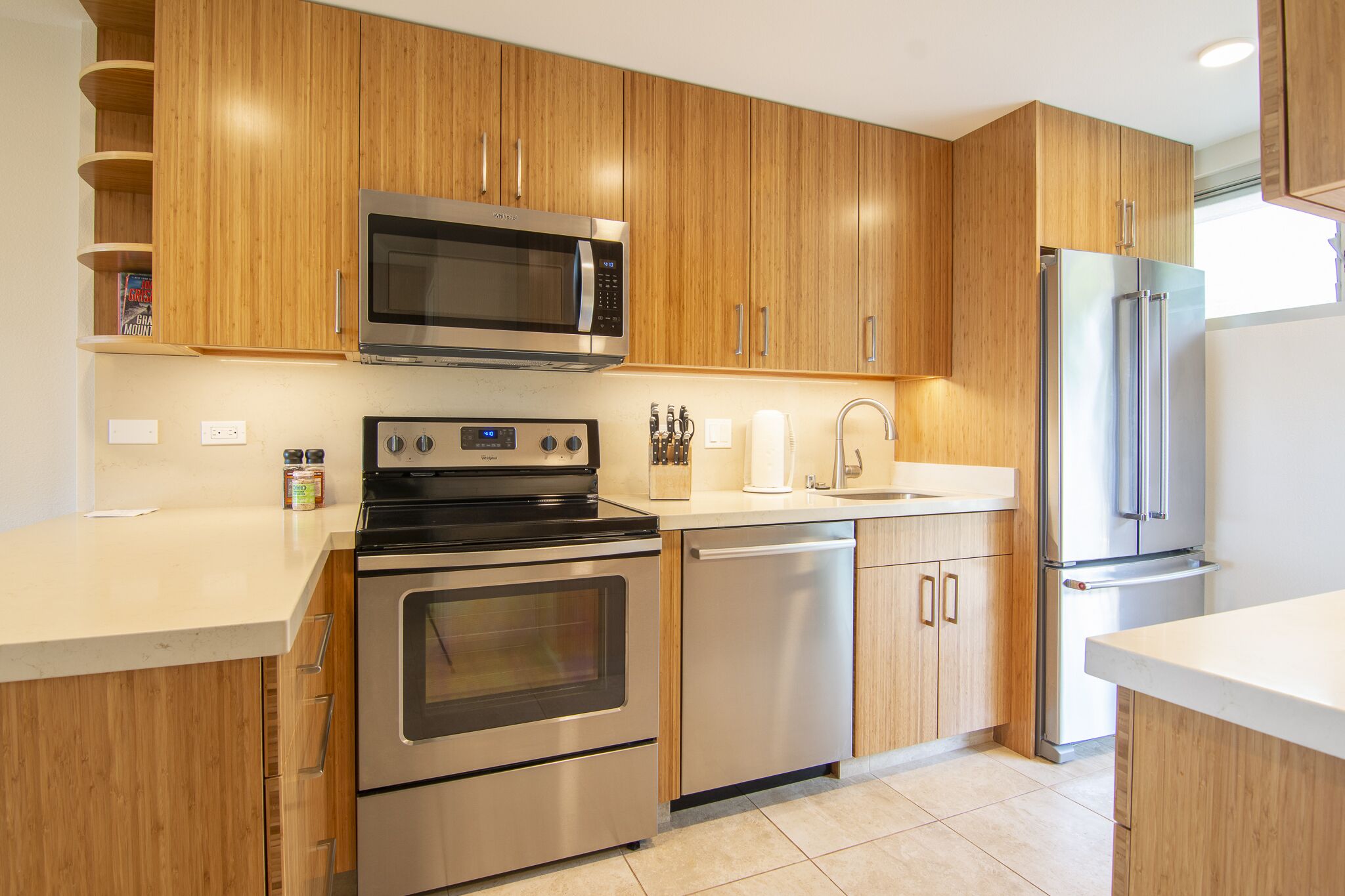 Una cocina moderna con gabinetes de madera y electrodomésticos de acero inoxidable, incluyendo microondas, horno, lavavajillas y refrigerador.