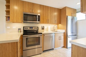 Una cocina moderna con gabinetes de madera y electrodomésticos de acero inoxidable, incluyendo microondas, horno, lavavajillas y refrigerador.